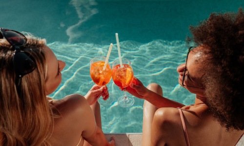 two people with drinks by a pool