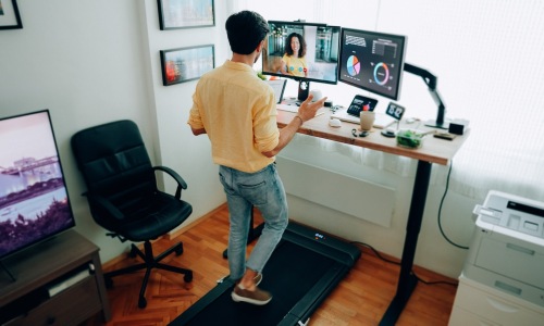 a person with a standing desk walking on a treadmill looking at multiple screens